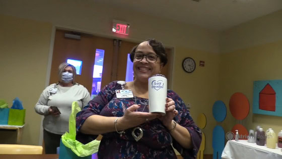 Smiling staff member holding a Culver’s cup during a Well‑Being Coaching Initiative graduation, with colorful wellness‑themed décor in the background.