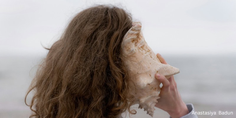 woman holding a conch shell to her ear